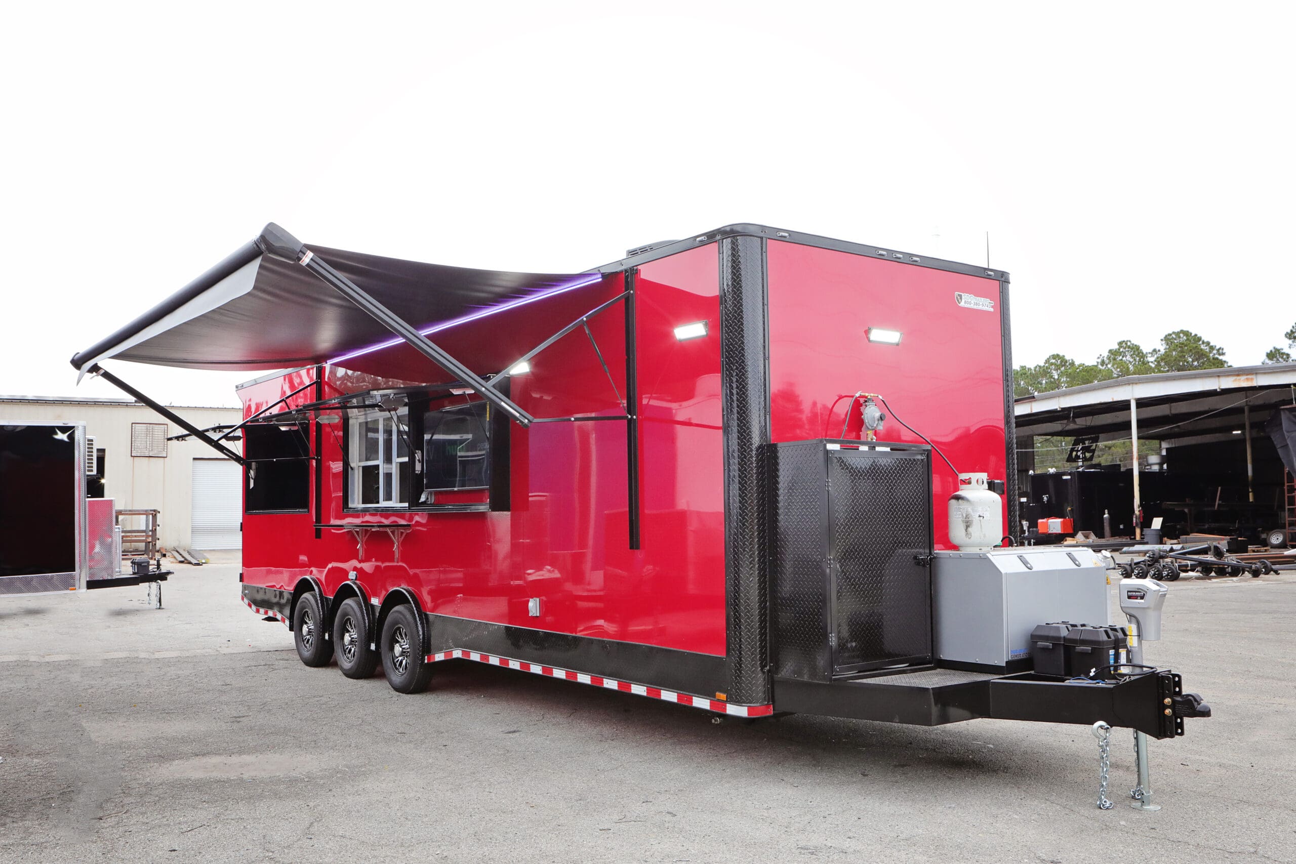 A red concession trailer with an extended awning and a propane tank on the hitch, parked outdoors.